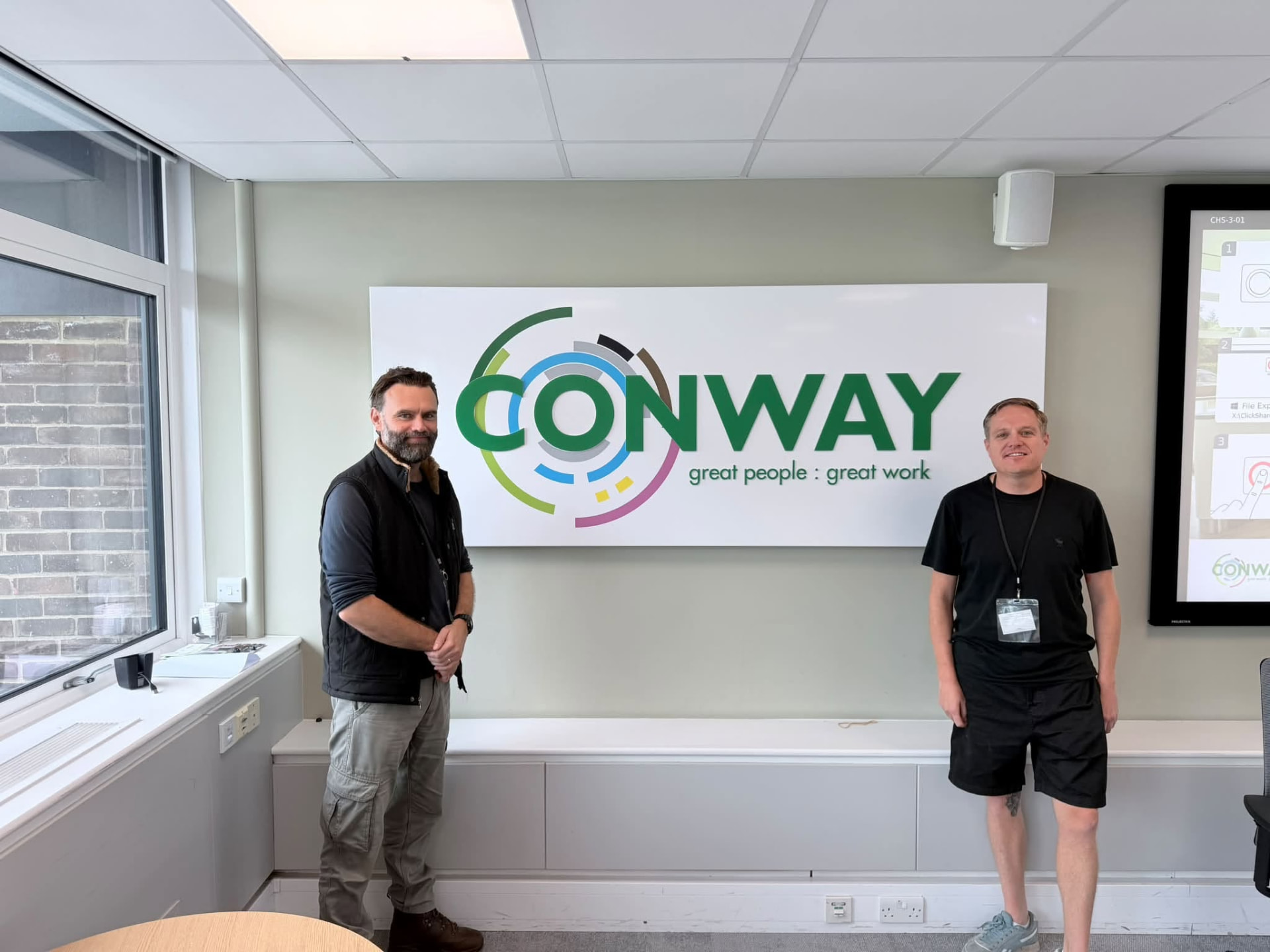 Two men from MENd Together and FM Conway standing in front of the FM Conway sign after the wellbeing session